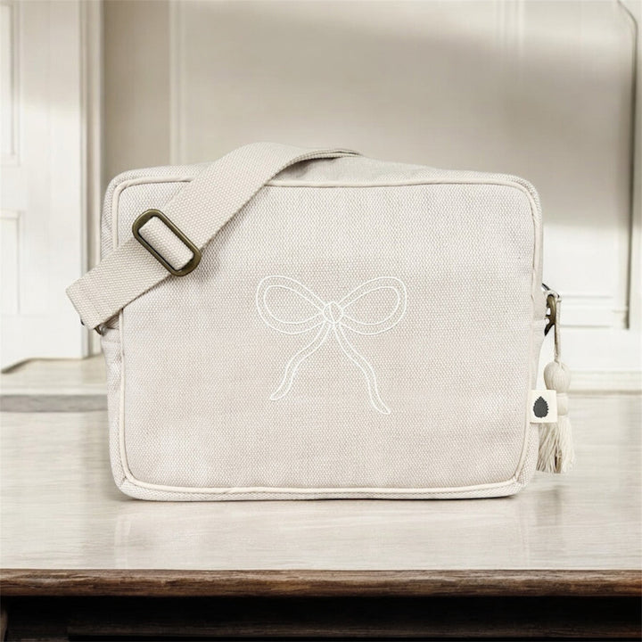 Mini changing bag in sand with bow embroidery on a table