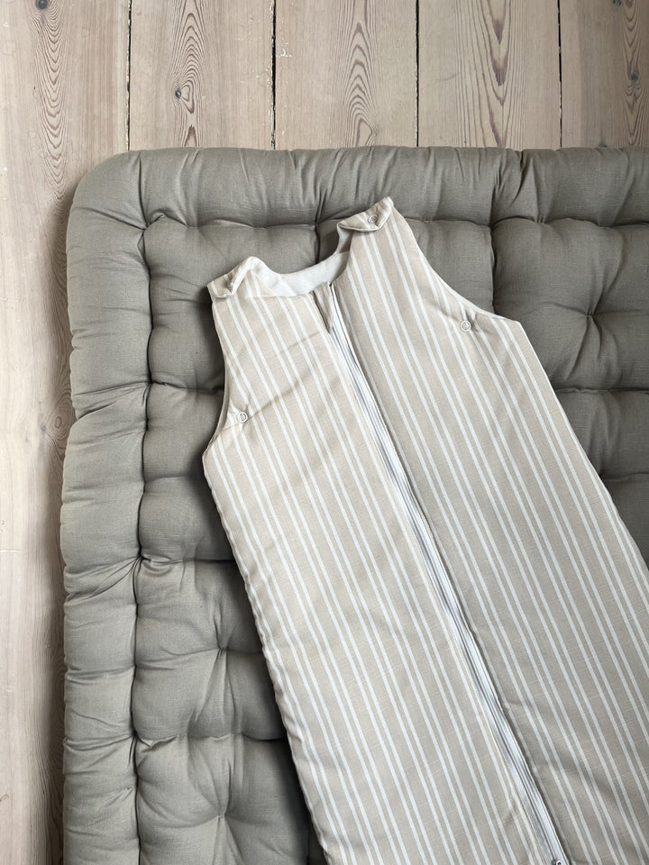 Beige Stripe sleeping bag for ages 0–6 months laid on a Mushroom play mat