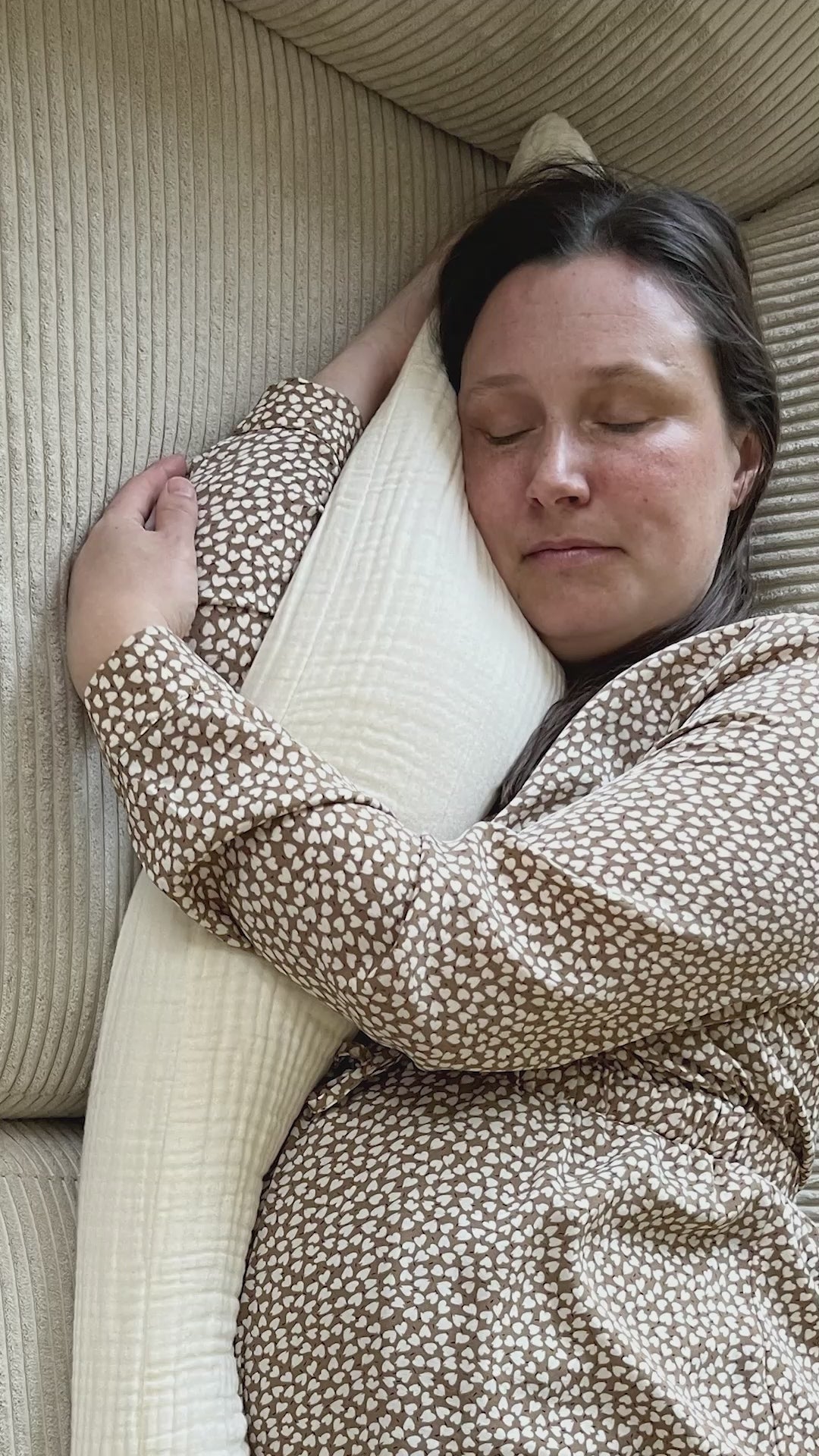 Kvinde slapper af med Kadera Mommy Pillow i cream på sofaen, hvor puden giver blød og behagelig støtte.